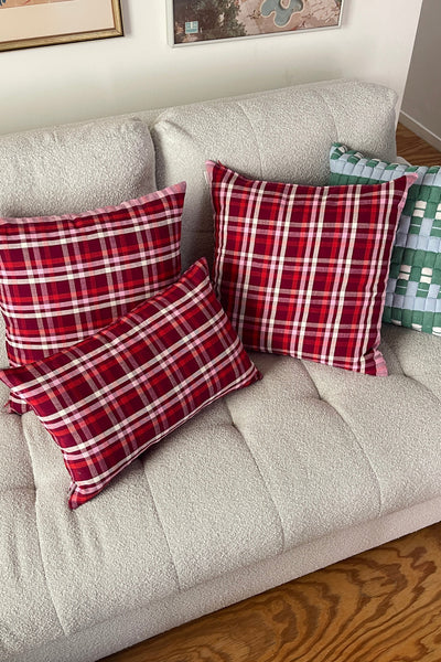 Red plaid pillows on a beige sofa with framed pictures in the background.