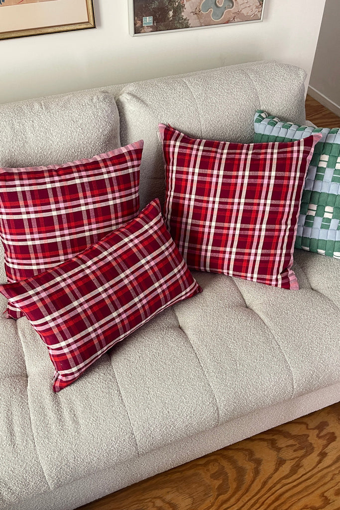 Red plaid pillows on a beige sofa with framed pictures in the background.